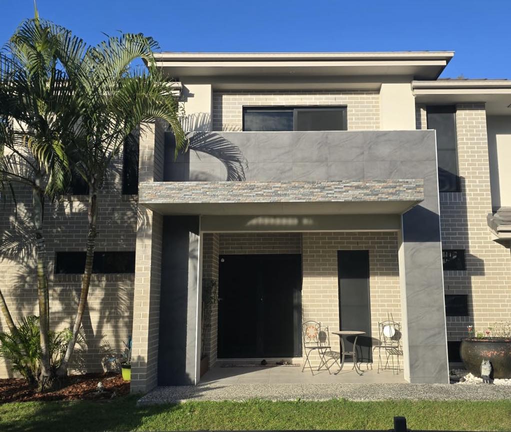 Modern two-story house with a driveway and palm trees on a clear day