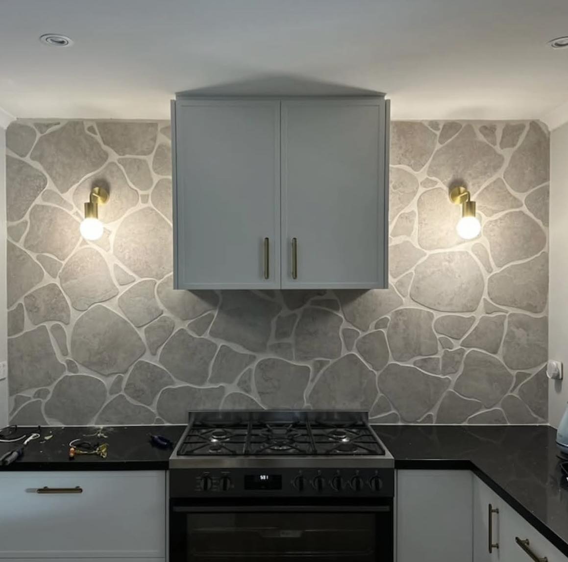 Modern kitchen with stone backsplash, gray cabinets, and black stovetop.